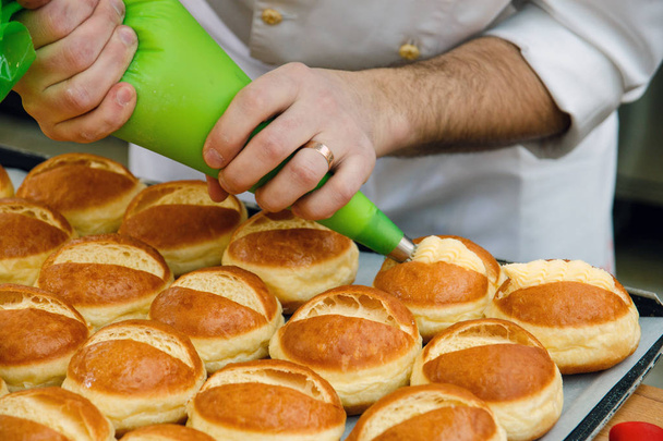 the pastry chef prepares the rolls and lubricate them with cream - Photo, Image