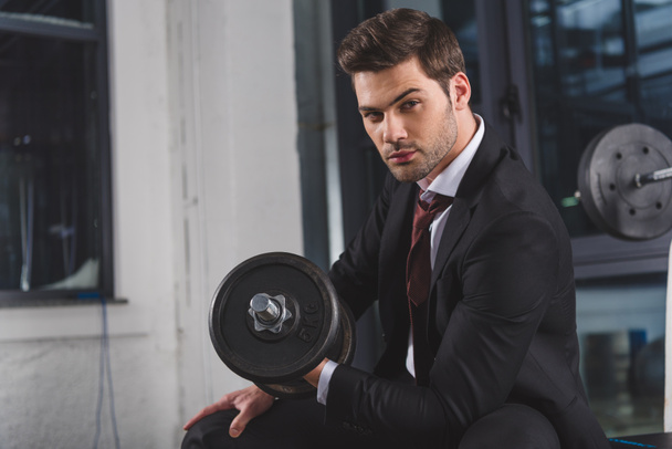 handsome businessman in suit training with dumbbell in sports center - 写真・画像