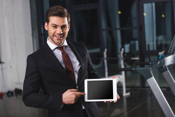 smiling businessman in suit pointing at digital tablet in sports center - Photo, Image
