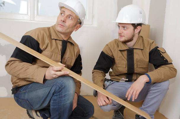 workmen crouching looking at floorboard - Zdjęcie, obraz