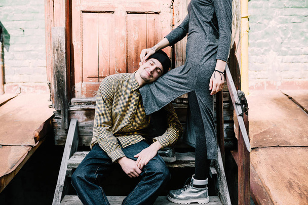 Smiling man with closed eyes leaning on girlfriend's knee at wooden stairway - Fotó, kép