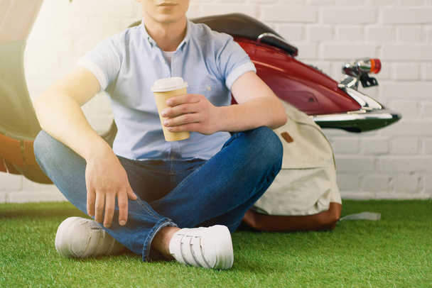 cropped shot of young man with cup of coffee to fo sitting in front of vintage scooter - Photo, Image
