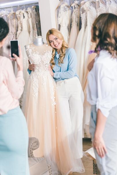 Bridesmaids and bride taking photo while choosing dress in wedding fashion shop - Photo, image