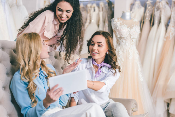 Atrakcyjne kobiety w wyborze sukni ślubnej i patrząc na tablecie w atelier ślubne - Zdjęcie, obraz