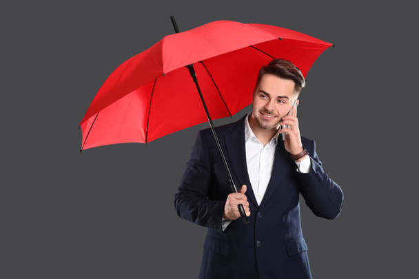 Fiatalember mobiltelefonján beszél piros esernyő  - Fotó, kép