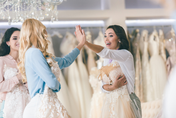 Young smiling brides giving high five in wedding atelier - Photo, Image