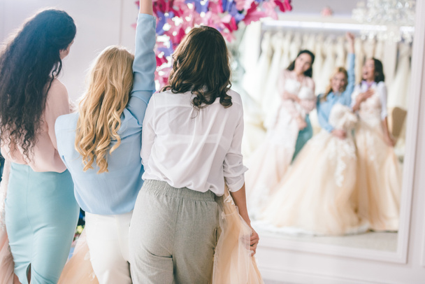 Привлекательная невеста и подружки невесты у зеркала в свадебном магазине
 - Фото, изображение