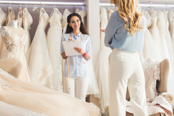 Beautiful bride and female tailor discussing dress design in wedding salon - Foto, afbeelding