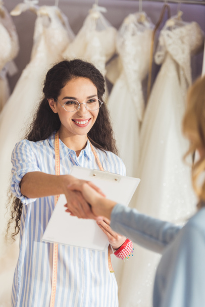 Femme tailleur et mariée serrant la main dans le magasin de mode de mariage
 - Photo, image
