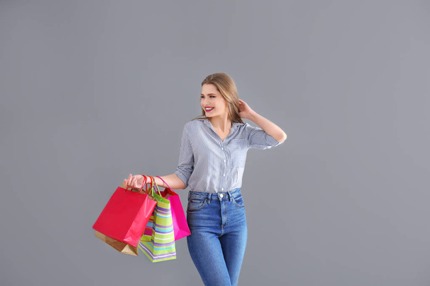 Beautiful young woman with shopping bags on grey background - Fotografie, Obrázek