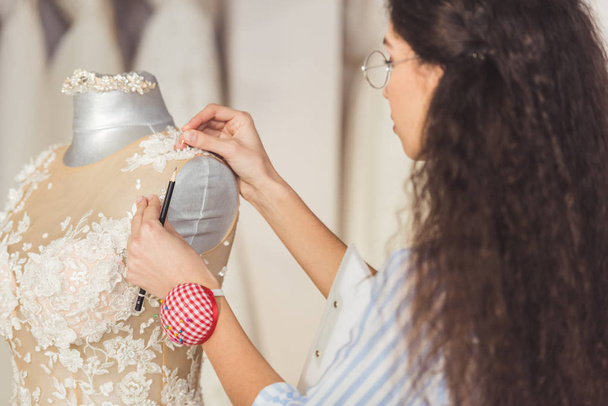 Nadelstickerin befestigt Spitzenkleid im Geschäft für Hochzeitsmode - Foto, Bild