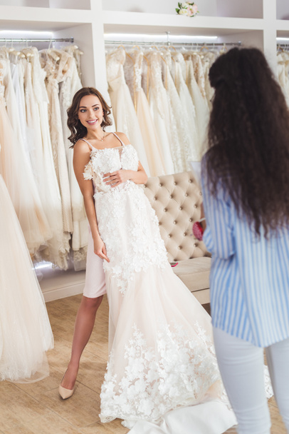 Female tailor by bride trying on wedding dress in wedding salon - Photo, image