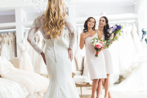 junge Braut und Brautjungfern mit Blumensträußen im Geschäft für Hochzeitsmode - Foto, Bild