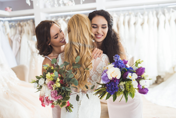 Attractive bride and bridesmaids embracing in wedding atelier - Photo, Image
