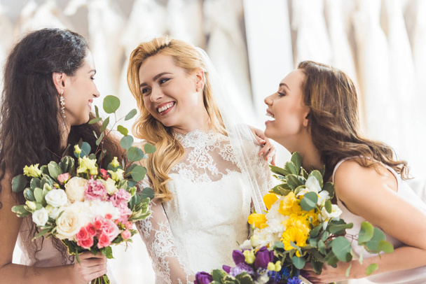 Noiva em vestido de renda e damas de honra com flores na loja de moda do casamento
 - Foto, Imagem