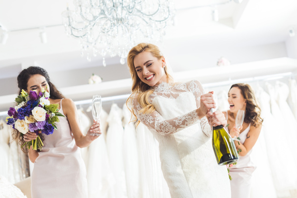 Attractive women in wedding dresses opening champagne in wedding salon - Фото, изображение