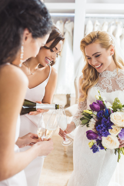 Attractive women in wedding dresses pouring champagne in wedding fashion shop - 写真・画像