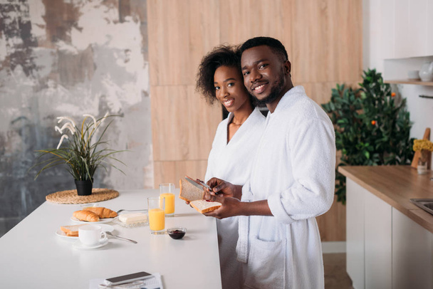 キッチンで朝食を持っているアフリカ系アメリカ人のカップルの笑顔 - 写真・画像
