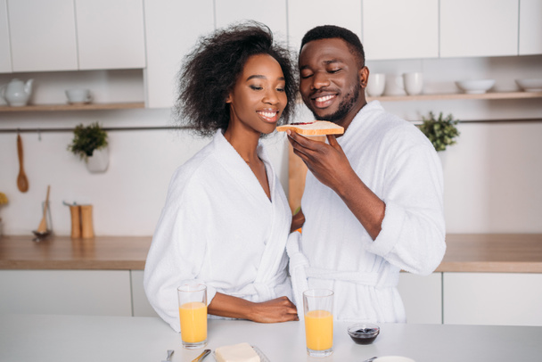 Smiling african american couple eating toast with jam in kitchen - Zdjęcie, obraz