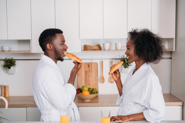 A fiatal pár, croissant-t eszik a konyhában oldalnézete - Fotó, kép
