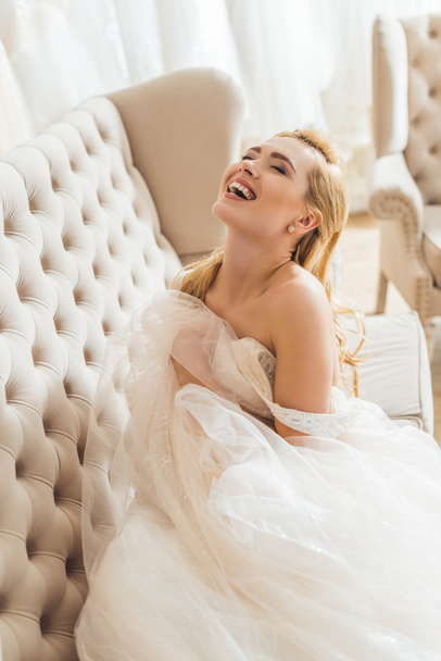 Beautiful bride in tulle dress on sofa in wedding atelier - Foto, imagen
