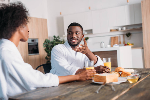 Smiling african american man talking to girlfriend while sitting at table with breakfast - Foto, imagen