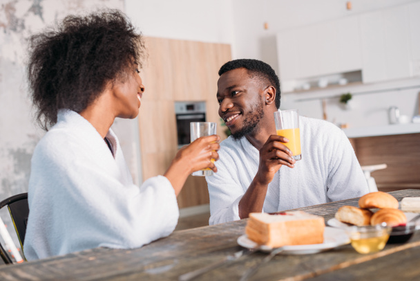 Jeune couple tenant des verres avec du jus et assis à table avec des toasts et des croissants
  - Photo, image
