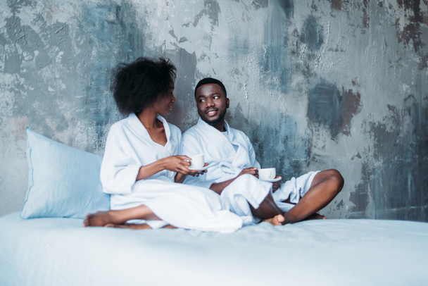 African american couple sitting in bed with cups of coffee - Fotografie, Obrázek