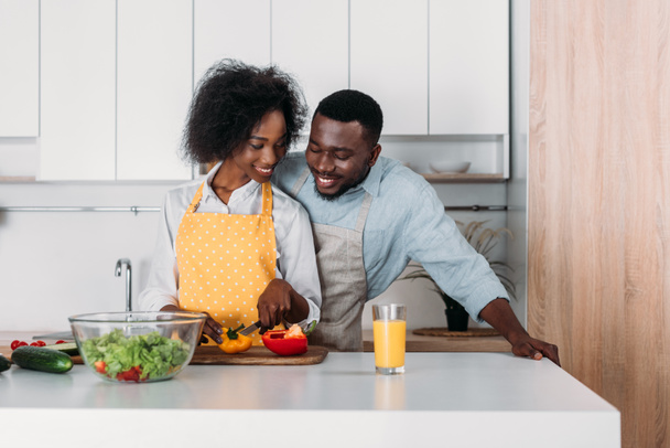 Afrikanisch-amerikanisches Paar in Schürzen steht am Tisch und kocht - Foto, Bild