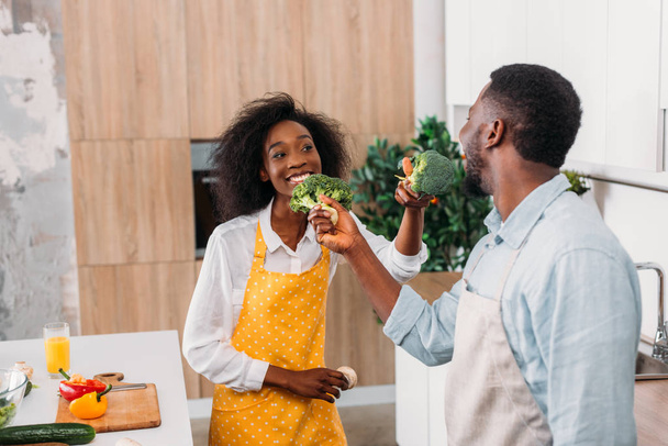 Sorrindo casal se divertindo com brócolis na cozinha
 - Foto, Imagem