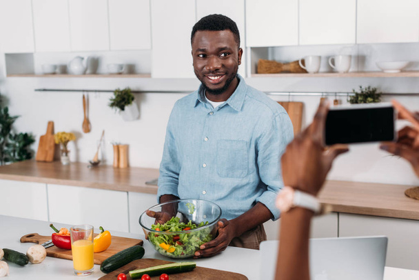 Cropped view of woman taking photo of boyfriend holding bowl with salad - Photo, Image