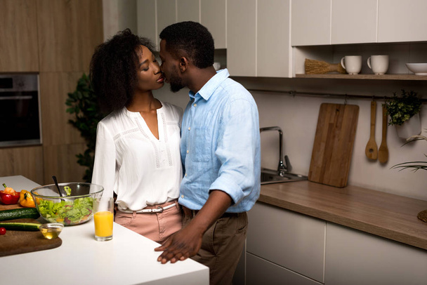 若いアフリカ系アメリカ人のカップルがキッチンのキス - 写真・画像