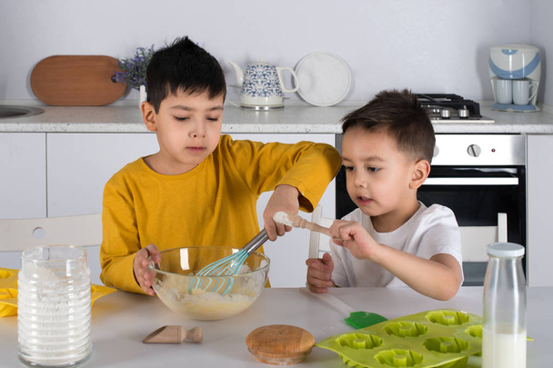 Δύο αγόρια μαγειρεύουν ζύμη για κέικ στην κουζίνα.  - Φωτογραφία, εικόνα