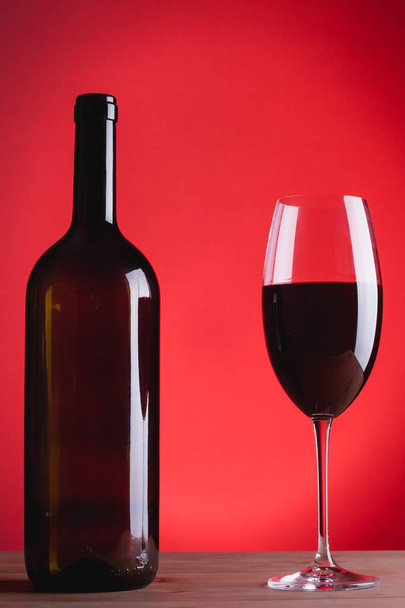 Flasche Wein und Glas mit Rotwein, auf rotem Hintergrund, - Foto, Bild