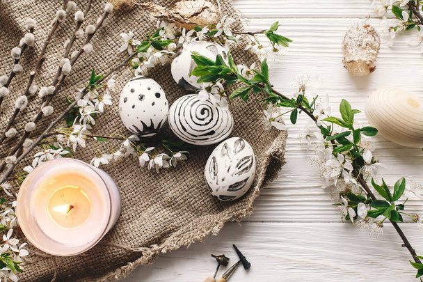 stylish easter flat lay. painted easter eggs black and white colors at rustic wooden background with spring flowers and candle. happy easter greeting card. modern easter eggs top view. - Φωτογραφία, εικόνα