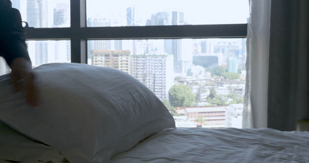 Fluffing kussens van de persoon op een bed met een stedelijke stad uitzicht vanuit de slaapkamer - Video