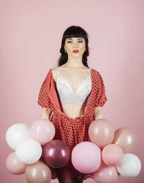 Sexy woman in white bra holds balloons on pink background. - Photo, Image