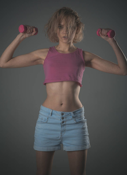 Woman coach with calm face holds dumbbells ?n grey background. - Foto, afbeelding