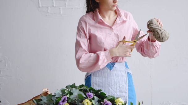 Front view of florist cuts a thread with scissors to arrange a bouquet - Фото, зображення