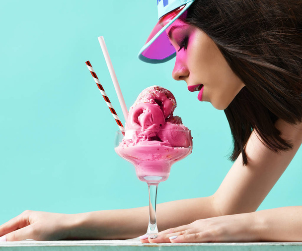 Young woman in pink hat eat strawberry ice-cream dessert on modern light blue  - Фото, зображення