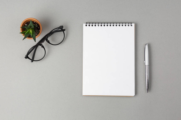 Notebook, pen, bril en groene bloem op een grijze achtergrond - Foto, afbeelding