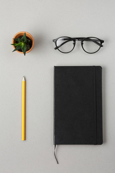 black notebook, pencil,glasses and green flower on a gray backgr - 写真・画像
