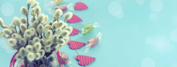 Banner feestelijke samenstelling in een glasvaas met twijgen bloeiwijzen. Heldere Candy slingers op een blauwe achtergrond. - Foto, afbeelding