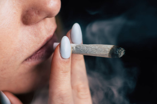 Cannabis weed, pali jointa w jego ręce A kobieta. Pali na czarnym tle. Pojęcia dotyczące używania marihuany i legalizacji konopi. - Zdjęcie, obraz