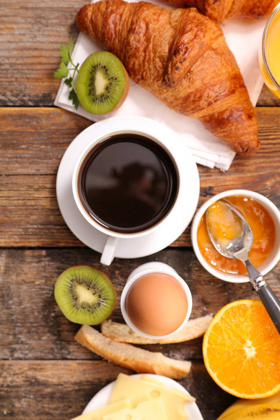 Breakfast with soft-boiled egg, croissants, coffee and fresh fruits on wooden table  - Photo, Image