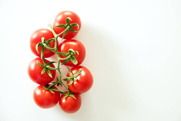 Minimalistic flat lay composition of shiny red cherry tomatoes reflecting light, laying on solid white table top. - Photo, image