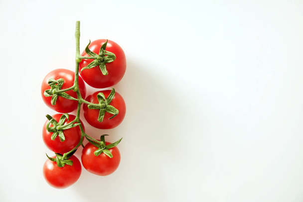 Minimalistic flat lay composition of shiny red cherry tomatoes reflecting light, laying on solid white table top. - Valokuva, kuva