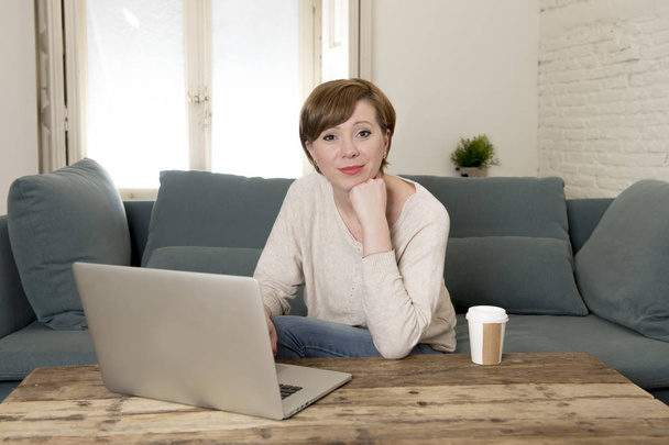 jonge aantrekkelijke en gelukkig vrouw aan huis banklaag doen sommige laptop computer werk glimlachend in ondernemer levensstijl ontspannen - Foto, afbeelding