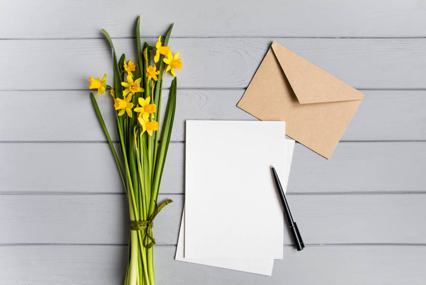 Letter, envelope and daffodils on grey background. Romantic holiday concept, top view, flat lay - Foto, Imagem