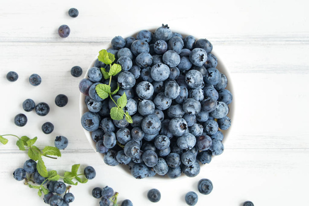 Fresh blueberries in white bawl on white wooden table. Flat lay, top view - Photo, image